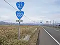 国道230号・国道37号との重複区間を示す標識、奥側に重複路線表示の案内標識・方面及び距離(106-A)(長万部町旭浜、2019年3月撮影)