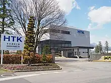 本社正門前(2017年4月)2022年に本多通信工業がミネベアミツミの子会社になったことに伴い、「HTK」ロゴの左隣に「MinebeaMitsumi」ロゴも併記されるようになる