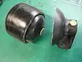 自動車（メルセデスベンツS123）のリヤサスペンションの油圧式レベライザシステムに使用されているアキュムレータをカットしたもの。内部の風船状のものがブラダ。右側の黄色い部分が給排油孔。