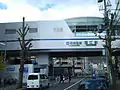 下り線のみ高架化された時点の駅舎　奥に旧上り線踏切（2015年12月）
