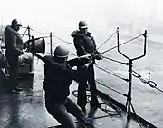 USS シャングリラ(CV-38)艦上にて、USS カルーザハッチー(AO-98)（英語版）に向けてスリングショット型索発射装置の試験を行う米国海軍兵達。最大射程は200フィート(約60m)であったという。(1963年)