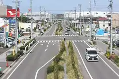 空港分岐線の分岐予定地(画像左)と愛知県道448号名古屋空港中央線(画像右)。25 mの広幅員道路の割に片側1車線となっているのは道路中央に名古屋高速の橋脚を建てるスペースを取っているためである(現在は片側2車線となっている。)。7次空整への対応による知事の一元化発表以後、費用対効果の面で県の外部監査やマスコミに取りざたされ、事業の妥当性に疑問が付された。