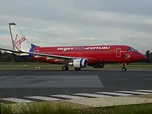 Mostly-red aircraft, with white fin and blue letterings, on ramp