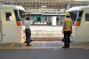 駅で先着列車に後着列車が連結（併合）する写真、左側の駅員が操車係として赤色と緑色の手旗を持って指示し、後着列車運転士に対して停止位置指示、小移動、連結通告、小移動の指示をしてその後連結される。