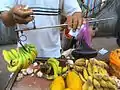 天秤ばかりの棒(天秤棒)と分銅を調整してバナナの重さを量る果物売り/中国海南省。