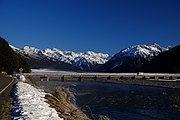 背景に冠雪した山をともなう、川にかかる橋の写真
