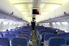 旅客機の客室内。中央の通路を挟んで座席が3席ずつ並んでいる。通路頭上にはディスプレイが配置されている。