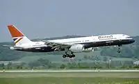 降着装置を下ろして飛行中の757を右側から見た写真。背後には草原の丘を望む。