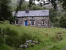 A colour photograph of a stone cottage on a hill