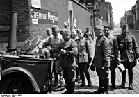 フィールドキッチンを使用するドイツ警察官、1940年に進駐先のフランスにて撮影。炊事係は白色の作業服を着ており、給食を待つ警察官たちは飯盒を手にしている。フィールドキッチンの側面には製造元の社名が書かれている（厨房機器や業務用洗濯機等のメーカであったゼンキンク社、1990年代に事業譲渡のためブランドが消滅）。