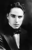 The black-and-white portrait of a young man. He is looking forward. He is wearing a black tux and a black bow tie.