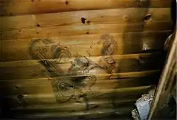  A wooden planked wall on which can be seen a stylised drawing of a woman's head and other ornamental shapes and objects
