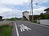 カーブミラーの右が一里塚跡の石碑。中央の建物の右手前の電柱が、左方向にある川辺橋方面から「くの字」なりに曲がった先にある最初の電柱。