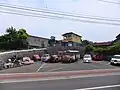 レストア待ちの車両。駐車場背後の縞模様の建物が博物館附属レストア工場