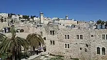 ヘブロン/アル＝ハリールの旧市街。地元の石灰石を使用した建築群からなる街並みと、その向こうに見えるイブラヒーム・モスク（ミナレットがある部分）/族長たちの墓。
