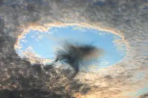 穴空き雲(円く空いている層の雲)と尾流雲(円い穴の直下に見える黒っぽい雲)オーストリアにて2008年8月撮影