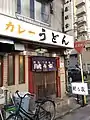 「本店 鯱乃家」の店舗外観。暖簾・路上看板は「鯱乃家」の名前となっているが、2階部分に取り付けられた看板は「若鯱家」のままである。2018年4月25日撮影。