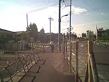 2004年9月における駅北口の都市計画道路。遠方に北口が見える。駅前広場から北に向かって500m程度の距離まで道路が整備され、未整備部には木杭と鉄線で囲われた「道路用地」が散在している。