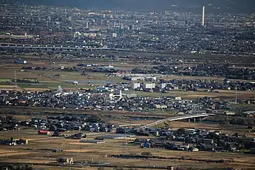 市街地があり、田園地帯があり、川と橋がある地方都市の風景ですが、画面の右上に白い棒が1本だけ立っているのが小さく見えます。それが、ソラエです。周辺に鉄塔やビルもあるのですが、高さのレベルが全然ちがいますので、ソラエだけが目立っています。