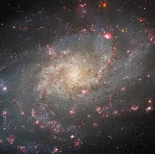アメリカ合衆国アリゾナ州キットピーク国立天文台にある Nicholas U. Mayall 4-meter Telescope で撮影された、渦巻銀河M33。赤い斑点のように見える部分はHII領域で、内部では盛んな星形成が行われている。銀河中心の右上に一際大きく見える赤い塊がNGC 604である。