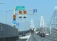 画像左:第二東名と伊勢湾岸道路の境界に設置された可変式速度規制標識と「ここから一般有料道路」の標識板（下り東海IC付近、KP30+649）。トレーラーの車線指定標識も設置された。画像右:可変式速度規制標識は平均1.3 km毎に設置されている。画像は高速車50 km/h規制時で、最低速度標識は消灯している。