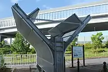 画像左:大型分岐型遮音壁の実物大モデル（豊田市花園町の若園緑地）。背後は当該遮音壁を用いた伊勢湾岸自動車道の豊田南IC付近。画像右:先端部をトナカイの角のように左右に分岐させることで、音の多重回帰、相互干渉作用を生じさせることで騒音を低減する。