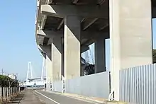 伊勢湾岸道路は愛知県など地元の強い要請によって建設された。このため国は、建設の見返りに費用負担など強い地元協力を要請した。画像左は新宝ふ頭に建設された新宝高架橋で、橋脚部分や東海IC料金所関係施設を除いて、高架下や両端の県道用地の取得費用は愛知県負担となった。画像右は名港潮見ICで、当該ICの建設費用は名古屋市と愛知県が全額負担のうえ、名古屋港管理組合が建設した。