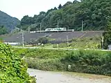 阿武隈川と兜駅。列車の左下にトンネルが木に半分隠れて見える（2006年10月）