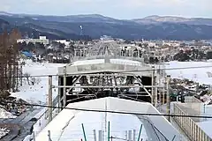海峡線の木古内駅方面を見る。奥には北海道新幹線の木古内駅の駅舎、手前のシェルターで覆われている所が北海道新幹線と在来線との分岐点である。在来線は新幹線の高架橋の両脇をスロープで下りS字カーブにより右に曲がりその後に左に曲がって木古内駅に繋がる。