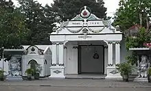 Front of white building, with two statues in front