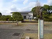 倉敷市真備ふるさと歴史館右手前に金田一耕助像と横溝正史疎開宅への案内板がある。