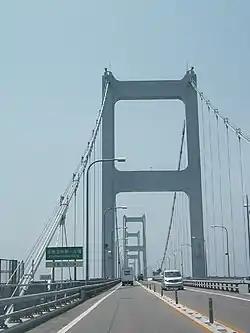 来島海峡第一大橋。"ステイロープ"とは写真手前左側の道路標識の後ろに見える垂直ではなくハの字に伸びる2本のロープ。その"ロッド"とはロープ下端の写真に映る白い筒状のものの更に下にある。破断したのは"センター"つまり中央支間のもの。