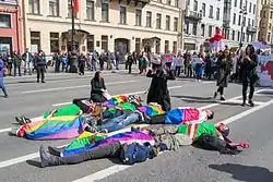 チェチェン人の母親が子供を悼む場面を演じる活動家。横たわった人々はLGBTとチェチェンの旗で覆われている。(サンクトペテルブルク、ネフスキー大通り2017年5月1日)