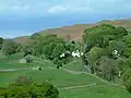 典型的な湖水地方の風景。ヒツジの放牧と石垣、山をバックにした白い家が見える。