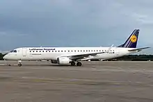 White and blue jet aircraft being pulled on ramp towards left under cloudy sky.