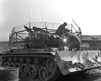 1953年3月25日、ドーザー付きのM46パットンの砲塔にバズーカ対策の金網を張っている海兵隊員。戦争終盤のこの当時には国連軍戦車は壕に待機し砲塔だけ出して砲撃支援任務を行うことが主体となっており、共産軍に鹵獲されたバズーカによる攻撃を受けて大きな損害を出していた。