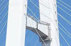 画像左 : 主塔上部は原則単ブロック溶接接合としたが水平梁上部はHTB接合である。ボルトで接合しているのが判る。画像右 : 下部工(基礎)の寸法を極力小さく抑えるために主塔下段水平梁以下をV字形に絞り込んだ。