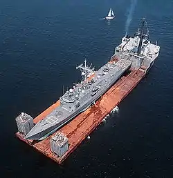 フリゲートを輸送する半潜水艇の画像。アメリカ海軍のミサイルフリゲート「サミュエル・B・ロバーツ (フリゲート)」(4,100 ロングトン) をドックワイズ社の半潜水艇「マイティ・サーバント2(en:Mighty Servant 2)」（29,193 総トン数）が（赤さびだらけで、載せた灰色一色の船との区別がはっきり付いている）甲板に載せている。画像は1988年（イラン・イラク戦争中）のもので、アーネスト・ウィル作戦中にペルシャ湾で機雷攻撃を受けて損傷した前者を母国へ帰還させようとしているところ。撮影地はドバイ沖。