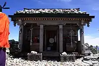 峰本社　神殿敷き詰められた玉石は、登拝者が現住地の近くにある河原から拾った石に願い事を書き、祈願成就のためここへ納めたもの。神殿右端の前にある平たく大きな石が雄山3,003mの基準になっている。左に写っている橙の衣は、登拝者へ登山安全を祈祷してくれる神職。