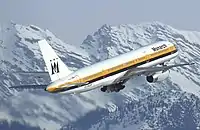斜め後ろから見た757の離陸の様子。背景には雪に覆われた山々が写っている。