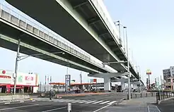 空港分岐線の分岐予定地(画像左)と愛知県道448号名古屋空港中央線(画像右)。25 mの広幅員道路の割に片側1車線となっているのは道路中央に名古屋高速の橋脚を建てるスペースを取っているためである(現在は片側2車線となっている。)。7次空整への対応による知事の一元化発表以後、費用対効果の面で県の外部監査やマスコミに取りざたされ、事業の妥当性に疑問が付された。
