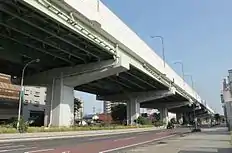 環状2号のPC連続ラーメン橋(左)と標準的なT字型橋脚の高架橋(右)。T字型では梁があるために道路長手方向の連続性が損なわれ、美的観点から好ましくないとされた。美的に良くないことは、用地買収を行うにあたって拒絶反応を示されかねないため、その対策としてPC連続ラーメン構造を採用することになった。