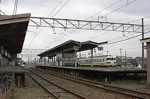 ホームと通過する北陸本線（撮影時）の457系（旧駅舎時代。2011年3月）