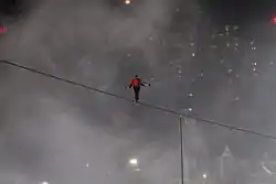 A man on a tightrope with mist and lights in the background