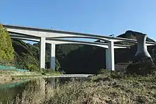 画像左 : 新安倍川橋と葵大橋。長さ1.7 kmのこの橋は県道と第二東名の二層構造で、画像奥の川岸に新静岡ICが敷設されている。インターを市街地から大きく外れた場所に造ったために新たな道路が必要になり、道路が増殖を続ける構図であるとして批判された。別のマスコミはこの橋を皮肉を込めて「土木技術の展覧会の面もある」と書いた。画像右 : 静岡市清水区和田島に架かる興津川橋。200以上の橋梁建設に関わってきた建設作業員は、山の中でこうした大きい橋を造るのは初めてで驚いたという。この橋の一山向こうに掘削された清水第三トンネルは公団が「第二東名の技術の結晶」と呼び、このトンネルの嘱託実験を請け負った大学教授が「唯一残った大規模な実験場だ」というインタビュー内容を皮肉交じりに記事化した。