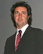 Photograph of an Italian male wearing a black suite and a white collared shirt.