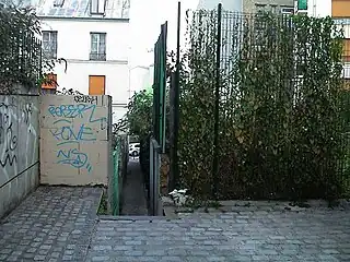 ピクセレクール通りに接続する, 拡張工事前のパサージュ・ド・ラ・デュエ (Le passage de la Duée, avant les travaux.)。道幅拡張前は80cm程で, 同1,80cmの5区シャ・キ・ペシュ通り (fr), 同1m程の12区サンティエ・デ・メリジエ (fr)・・等と共に, パリ市内の最も道幅が狭い通りの一つだった。