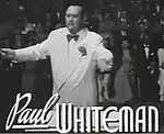 ワーナーブラザーズ映画『Rhapsody in Blue』（1945年）に出演する"ジャズの王"ポール・ホワイトマン。 映画『Rhapsody in Blue』予告編を閲覧するホワイトマンの依頼でガーシュウィンの楽曲『ラプソディ・イン・ブルー』は作曲された。 楽曲『ラプソディ・イン・ブルー』1924年版を試聴する