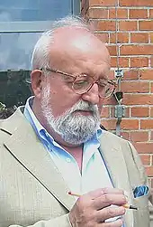 白い髭の男性。眼鏡をかけて青色のシャツを着ている。