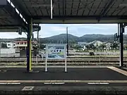 駅名標(2018年5月、菜の花と駅前広場の足湯を描いたもの)